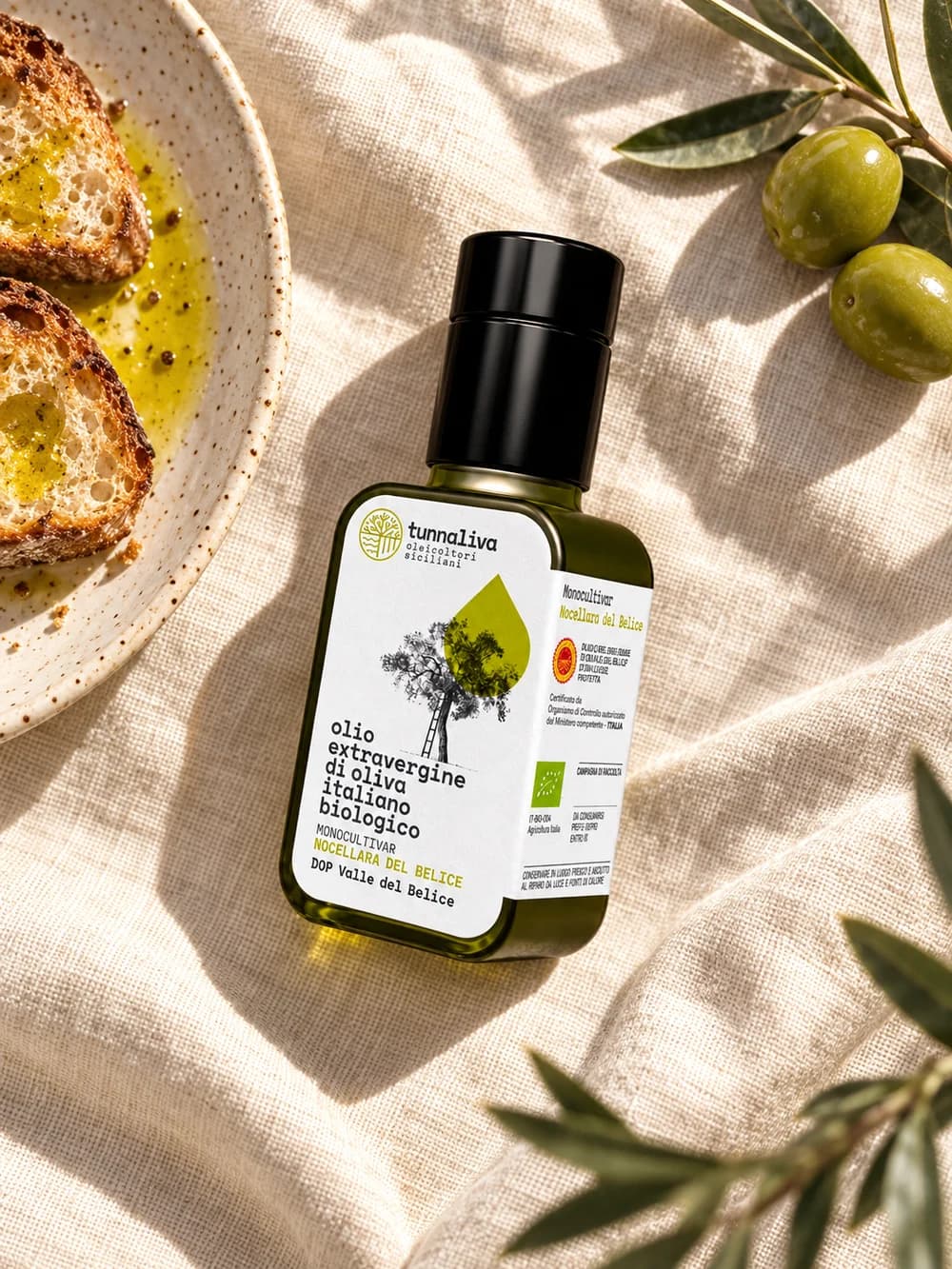 Piccola bottiglia di olio accanto al pane su lino chiaro