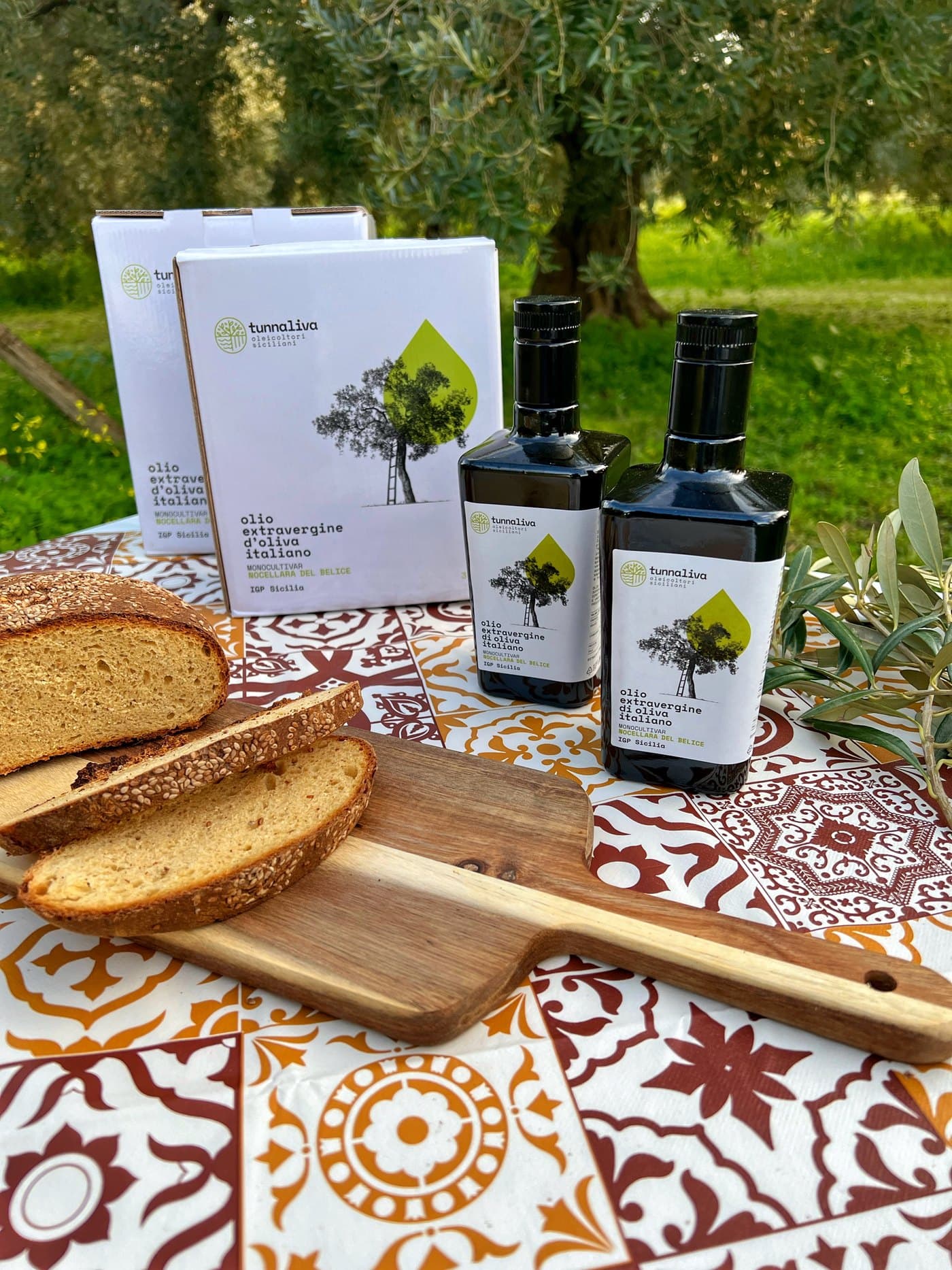 Pan recién cortado y botellas de aceite sobre una mesa de mayólica siciliana